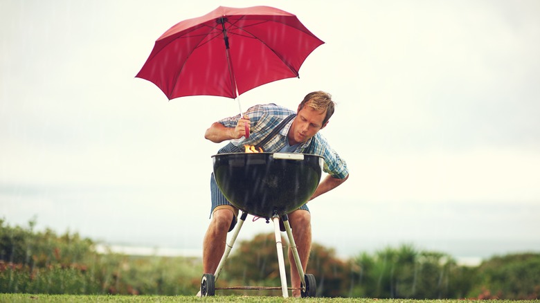 Man holding umbrella over grill