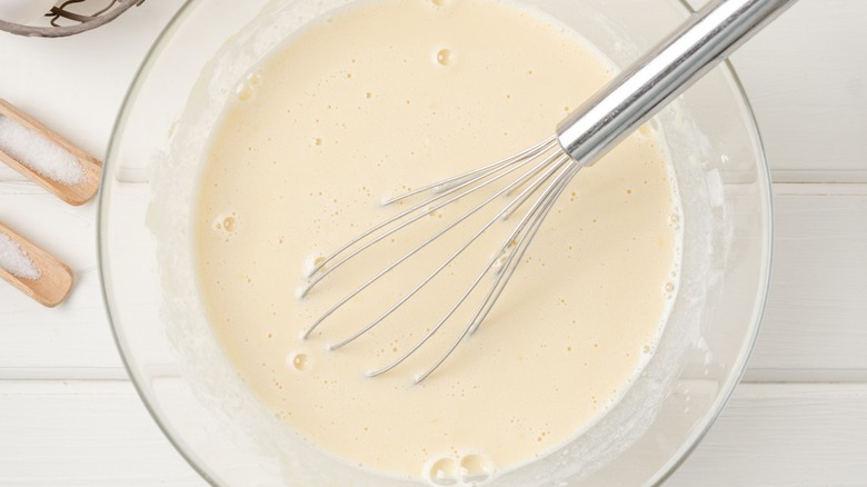 A whisk sits in a bowl of buttermilk next to the sallt