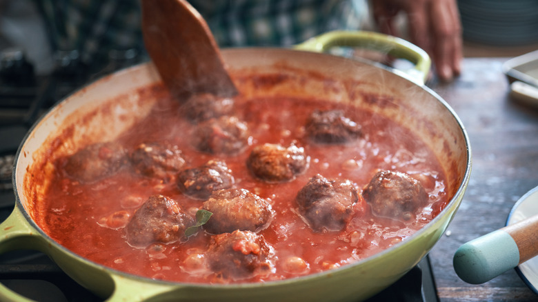 Person cooking meatballs and sauce