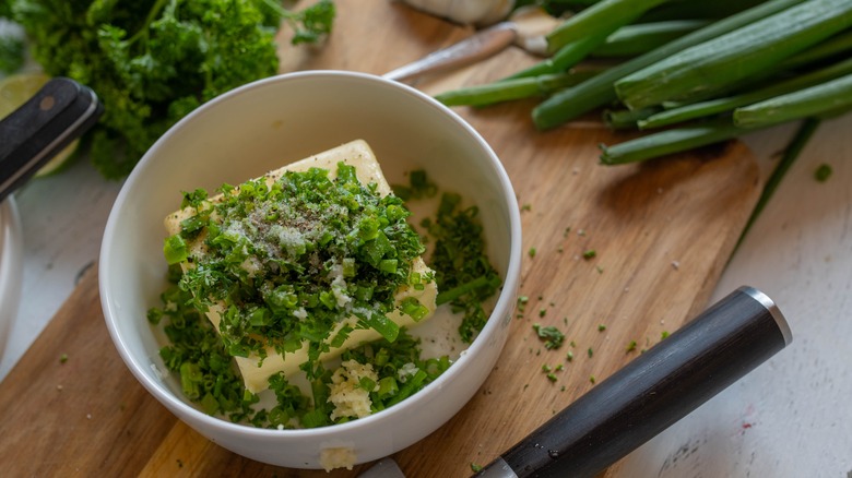 Block of butter with chopped herbs and seasonings in a bowl