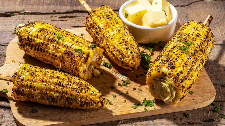 Grilled corn on the cob with a small bowl of butter on a wooden board