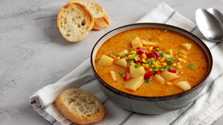 corn chowder in a bowl with sliced bread and spoons on the side