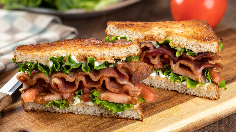 A bacon, lettuce and tomato sandwich cut in half on a wooden cutting board