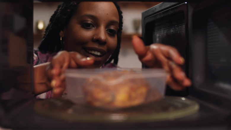 A woman heats chicken in microwave
