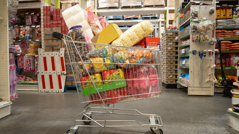 A metal shopping full of various items sitting unattended in between grocery aisles