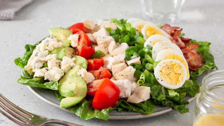 Cobb salad on a white plate against a gray speckled background