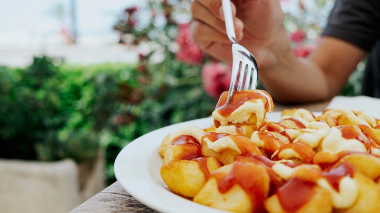 Closeup of a man using a fork to eat patatas bravas