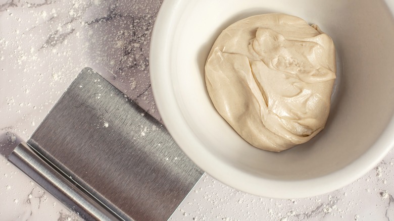 A dough scraper beside a tidy bowl of dough.