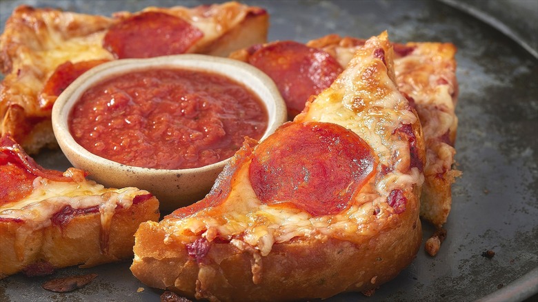 Sliced pizza toast with pepperoni served with a cup of tomato sauce