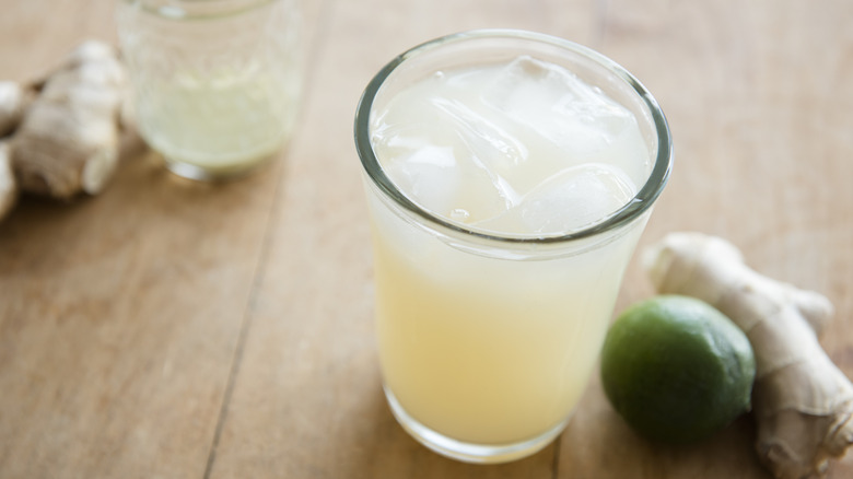 A glass of ginger ale with lime and ginger on the side