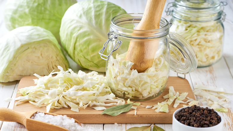 Preparing sauerkraut with jar, surrounded by ingredients