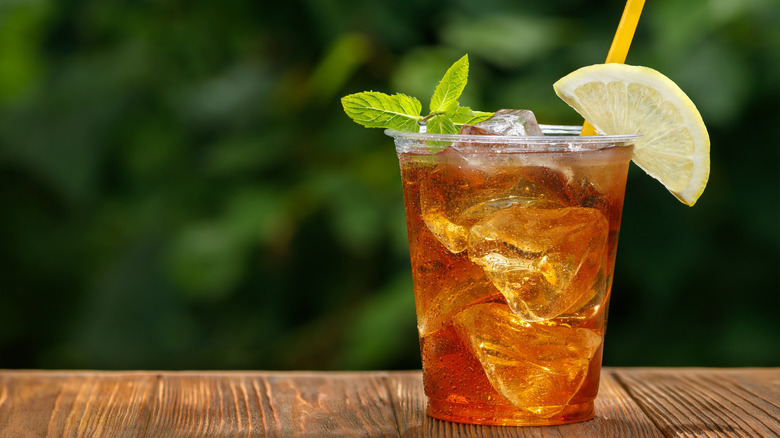 Cup of iced tea with lemon and mint garnish sitting on a wooden table outside