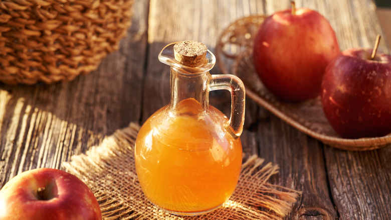 A bottle of apple cider vinegar and apples on a table