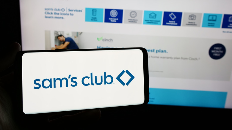 Sam's Club app on phone in front of a computer screen with the Sam's Club website open