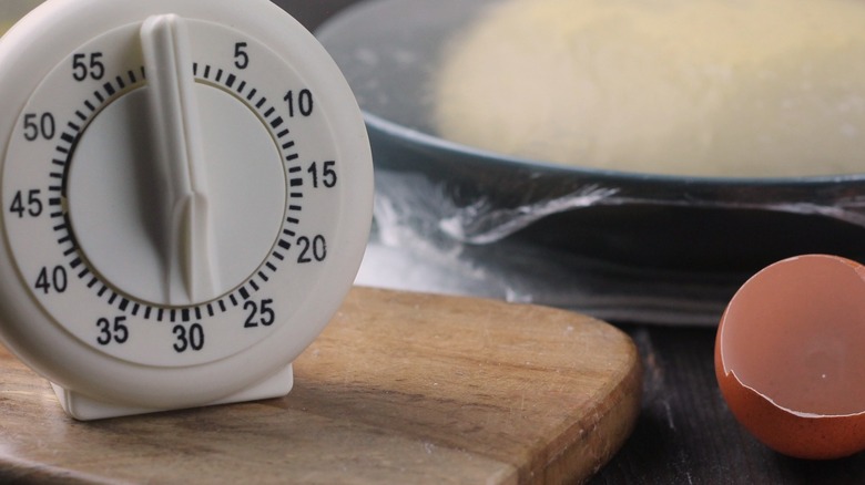 White egg timer sitting next to cracked egg and proofing dough