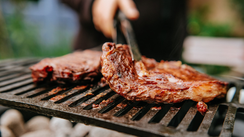 Steak being picked up from a grill.