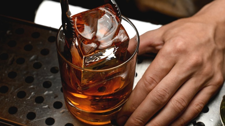 Bartender adding an ice cube into a glass of bourbon