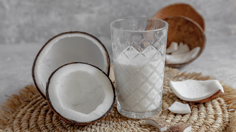 Split open coconut next to glass of coconut milk