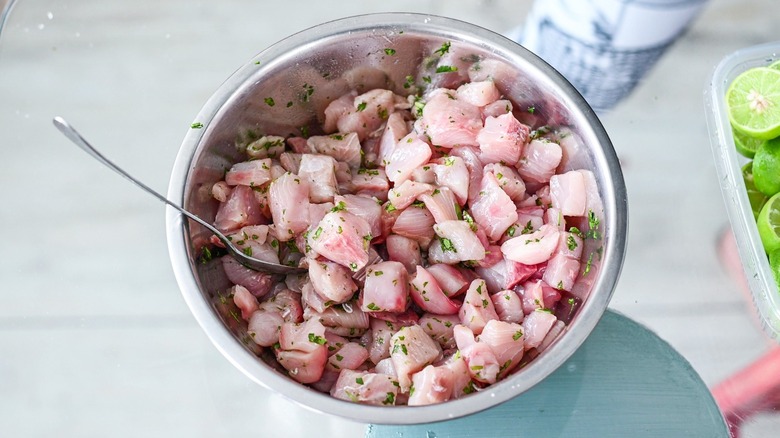 Ceviche is mixed in a metal bowl with seasonings.