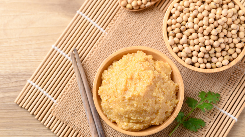 Miso paste in a wooden bow sitting next to a bow of soybeans.