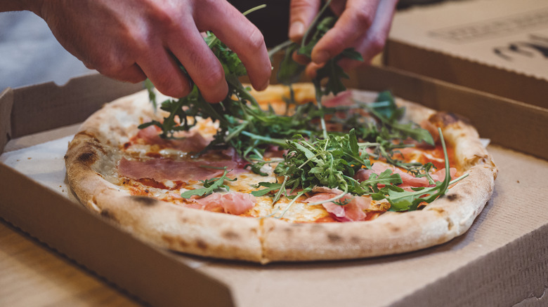 Person adding arugula to pizza