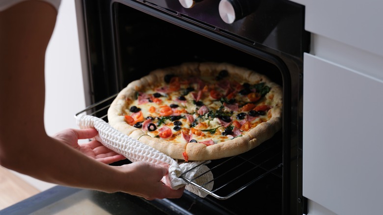 Person putting pizza in an oven