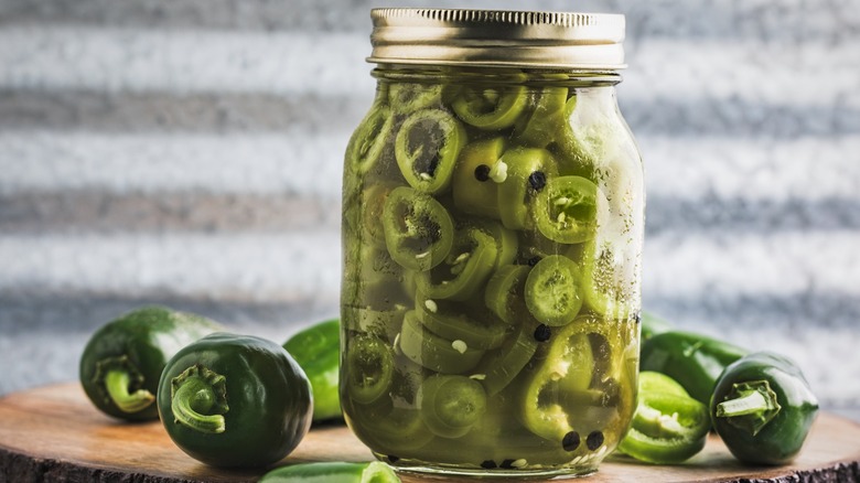 Jar of pickled jalapeños surrounded by fresh jalapeños