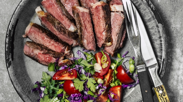 Sliced steak and side salad on a plate with fork and knife