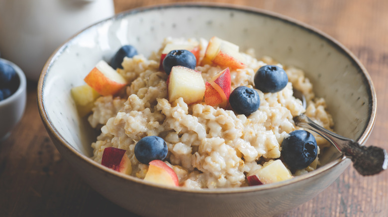 A bowl of oatmeal with apples and blueberries on top.