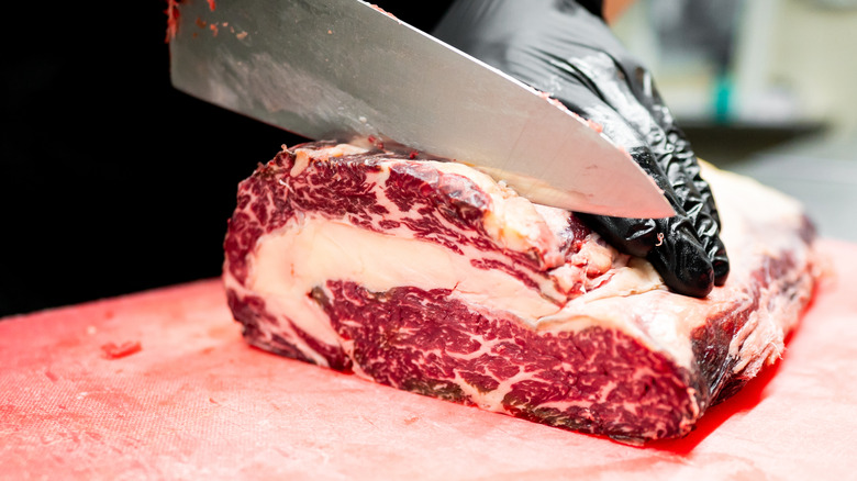 A close-up of a butcher slicing through a cut of steak.