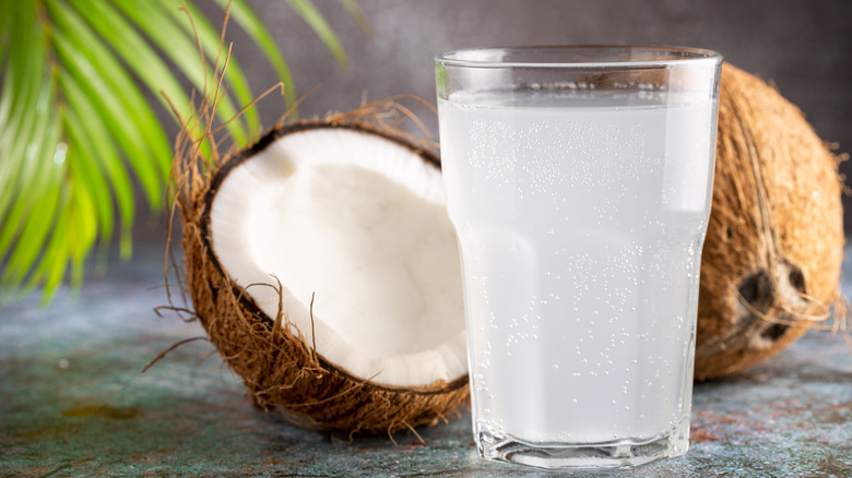 Glass of coconut water with a halved coconut