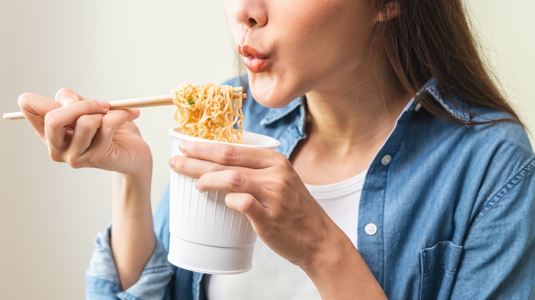 Person eating cup ramen with chopsticks