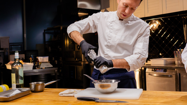 Chef salting food in stainless steel bowl