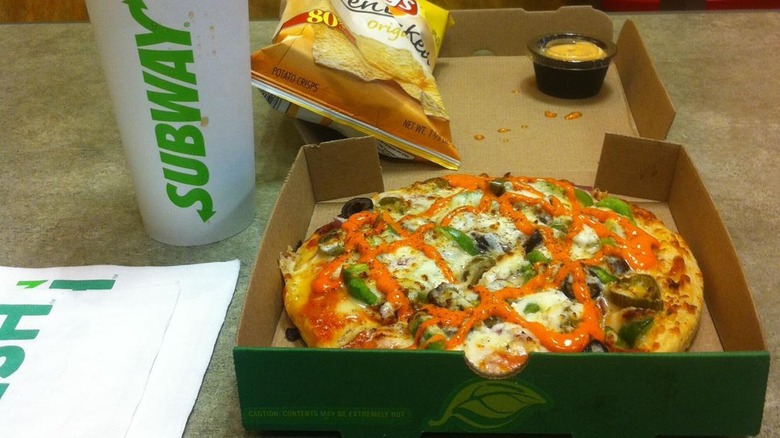 A Subway pizza next to chips and soda