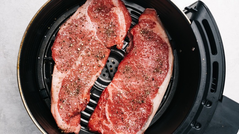 Two raw seasoned flat iron steaks in an open air fryer basket