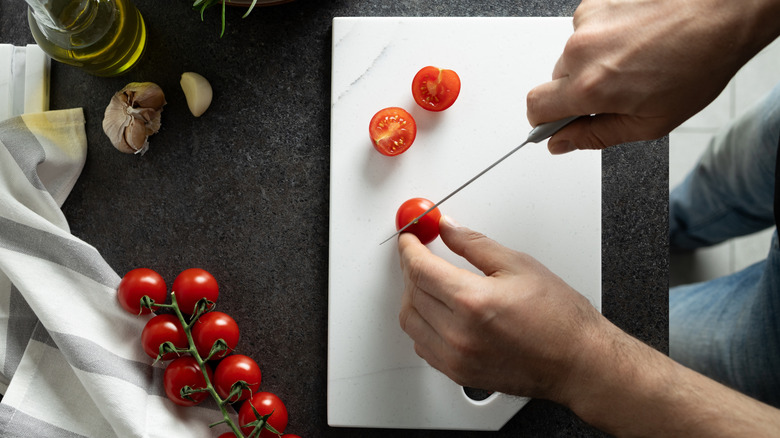 person cutting tomatoes on a marble cutting board