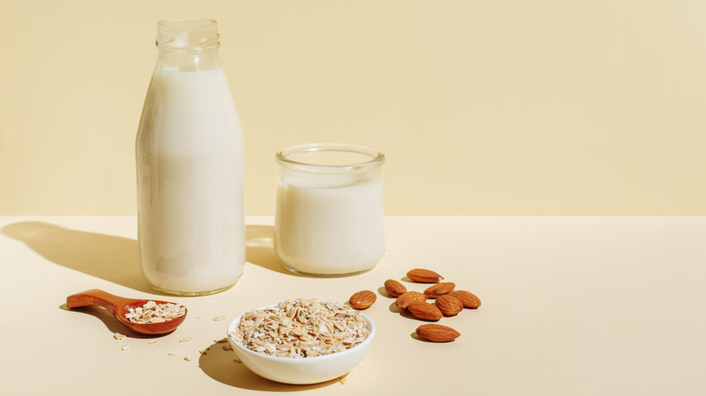 A bottle a glass of non-dairy milk with a bowl of oats and almonds on the side