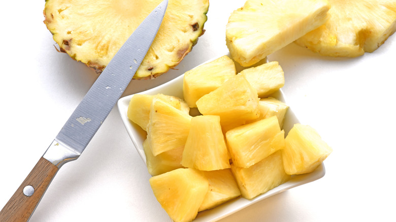 A knife sits with cut and sliced pineapple pieces