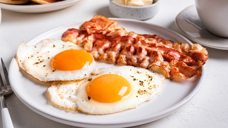 Two sunny side up eggs on a plate with bacon