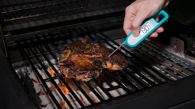 person checking steak temperature on grill