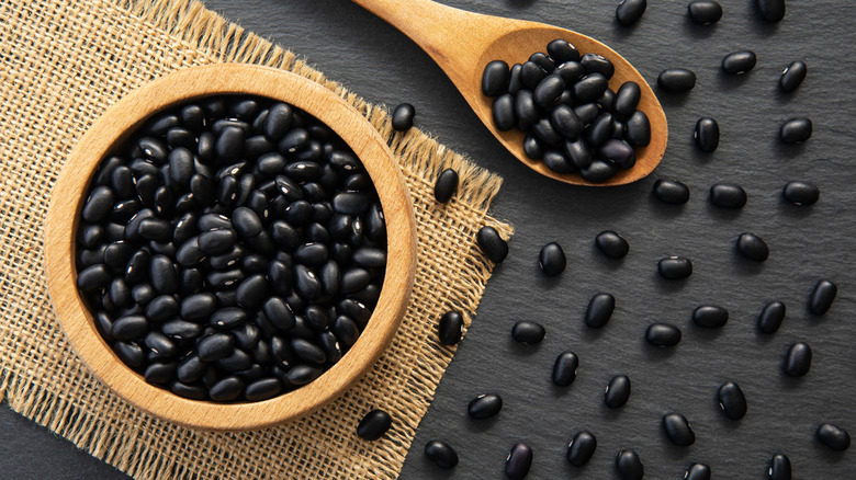 Wood bowl of dried black beans with wooden spoon on a natural matt