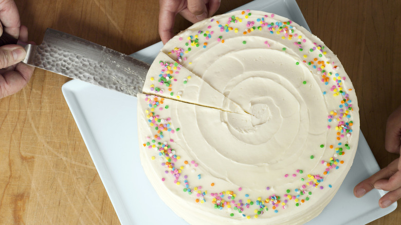 Cutting a vanilla cake with colorful sprinkles