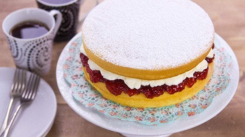 Victoria sponge cake on platter with tea and plates