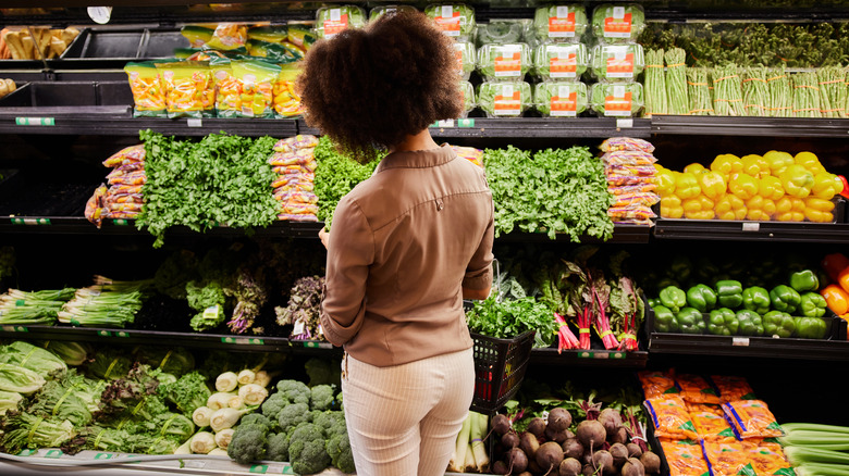 Person standing in front of shelves of fresh vegetables