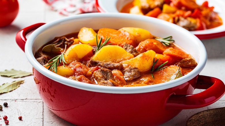 Beef stew with potatoes, carrots, and fresh herbs in a red pot