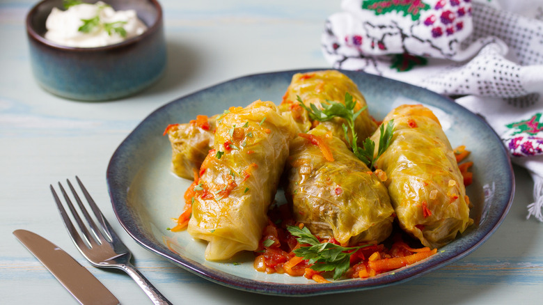 Plate of cabbage rolls, cutlery, and a small ramekin of sour cream