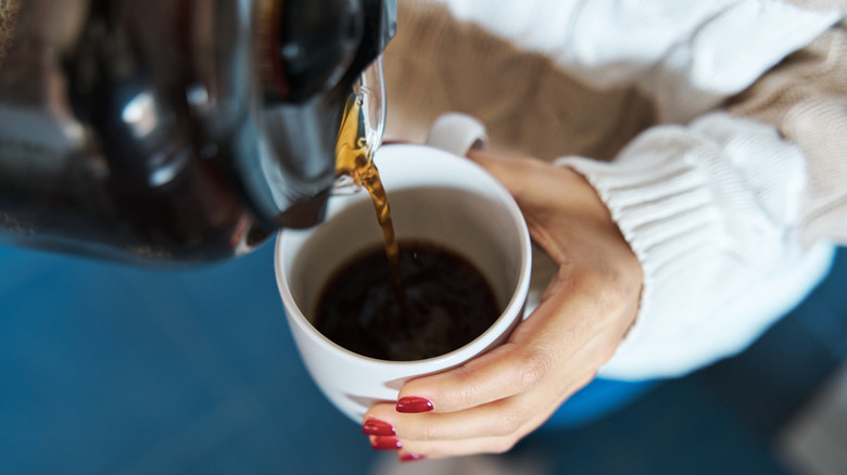 A person with red fingernails pours a mug of drip coffee