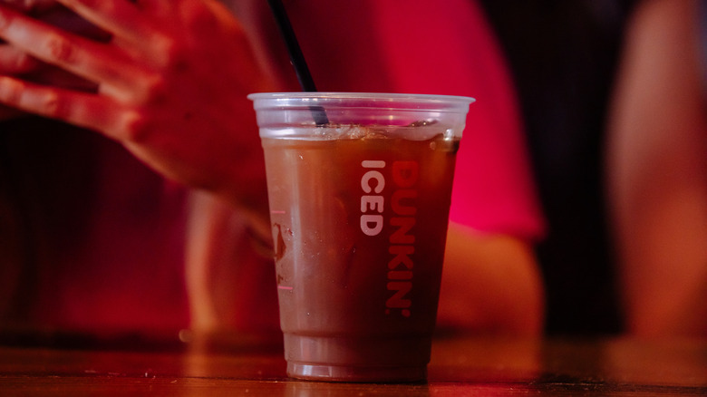 A cup of Dunkin iced coffee sits on a counter in front of blurred figures