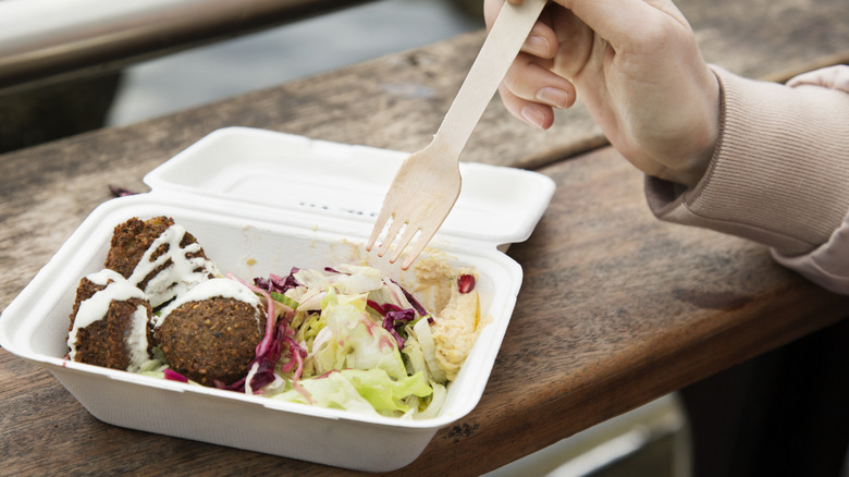 Person eating falafel from a styrofoam takeout container