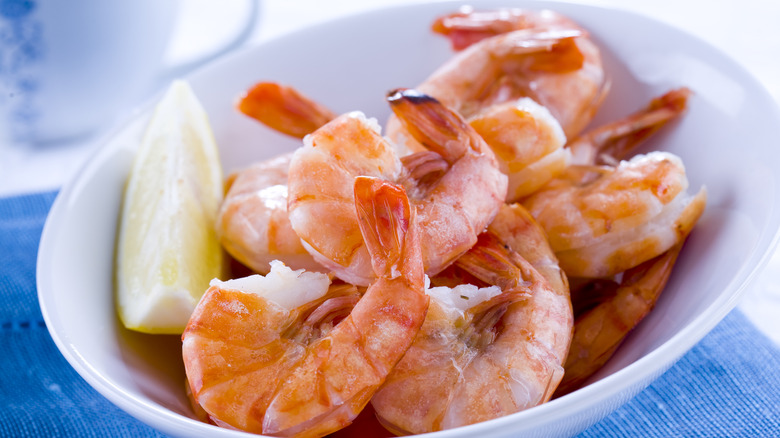 A bowl of shrimp with a lemon slice.